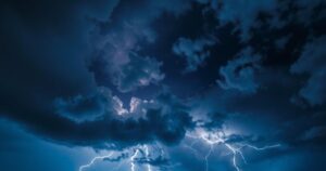 Partly cloudy night sky with dark clouds and distant lightning, reflecting the weather forecast for thunderstorms.