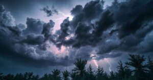 Storm clouds with lightning over trees in a rural area, depicting a strong thunderstorm scene.